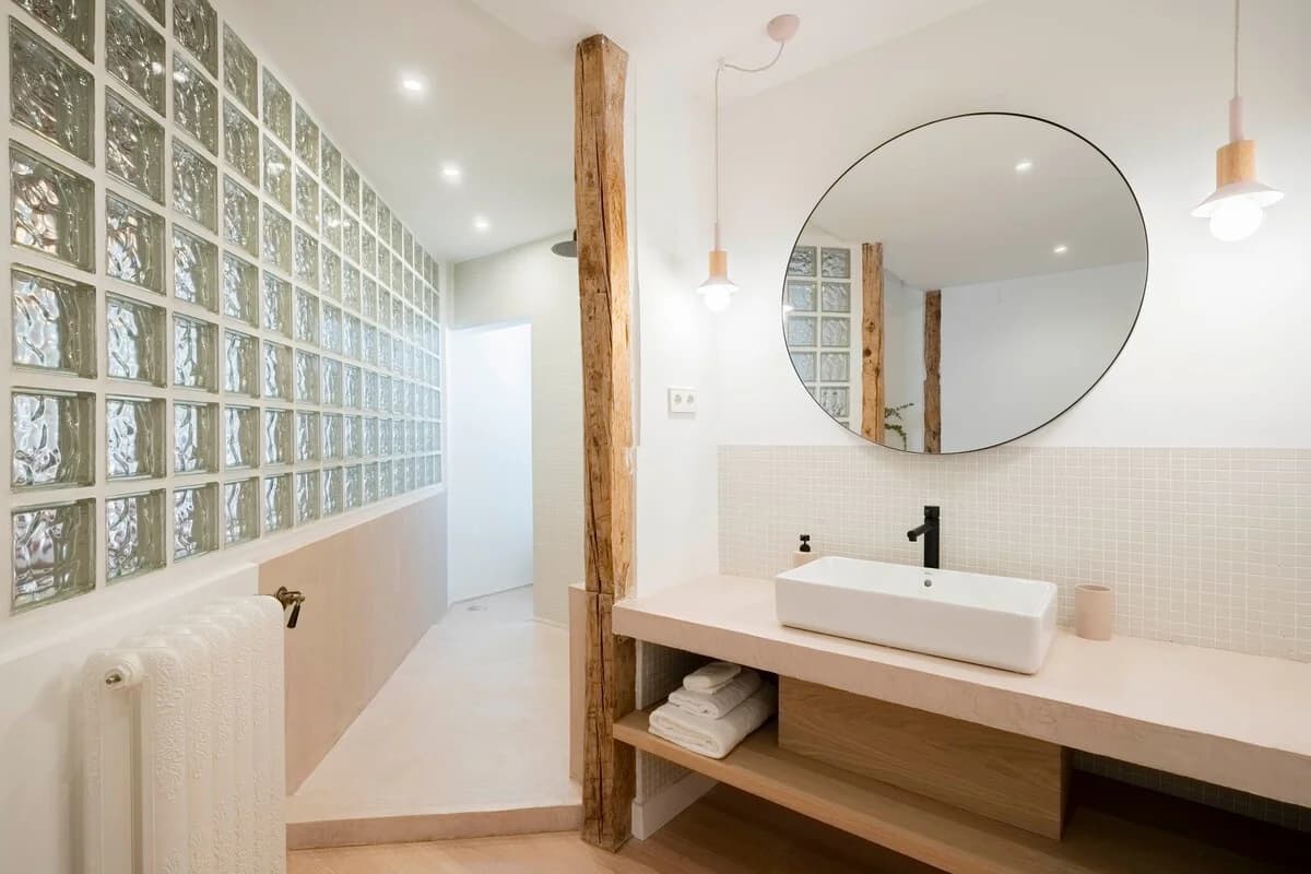 Spa-like bathroom with round mirror, glass-block wall and reclaimed beam