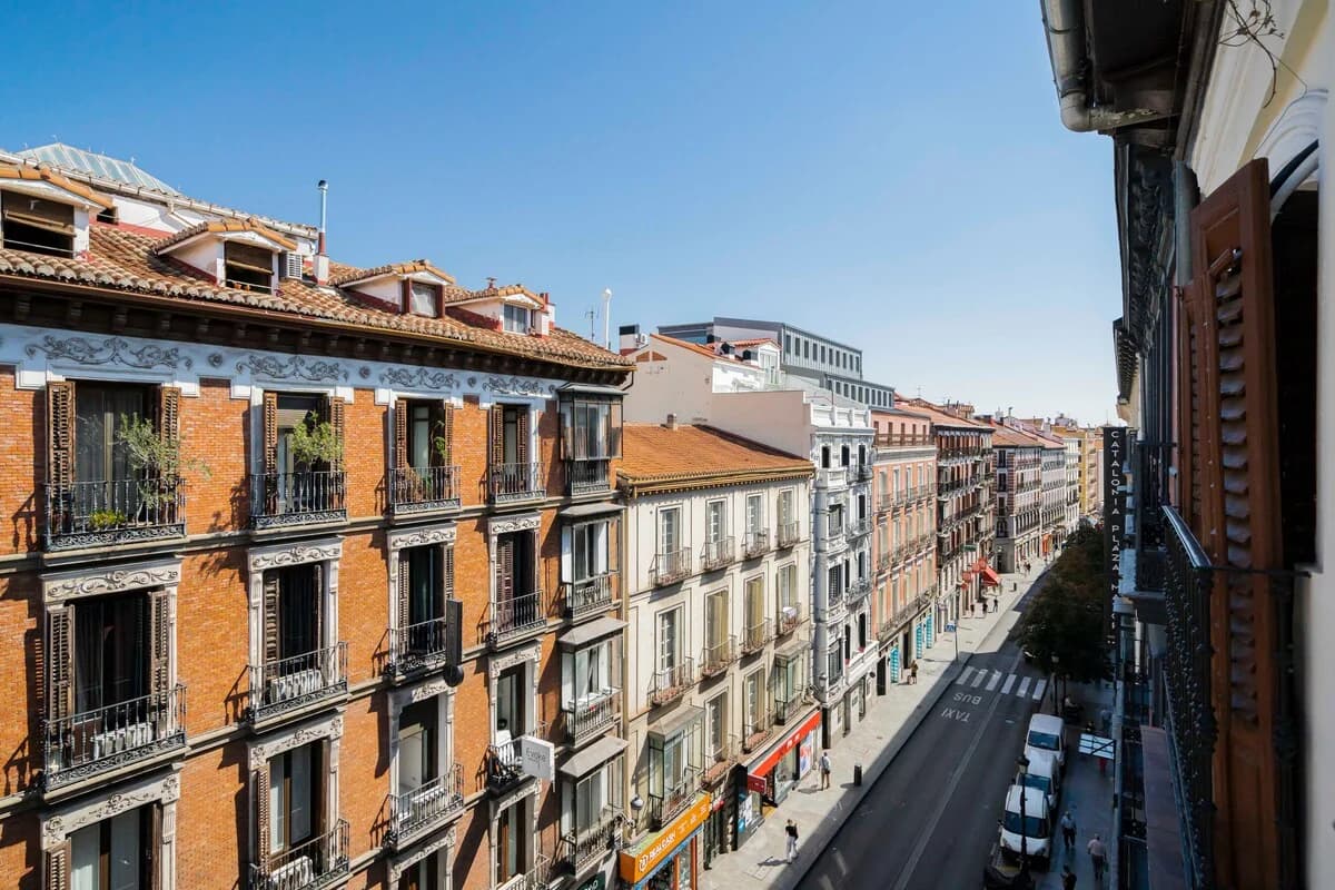 Shuttered balcony view down a sunlit Madrid avenue from above