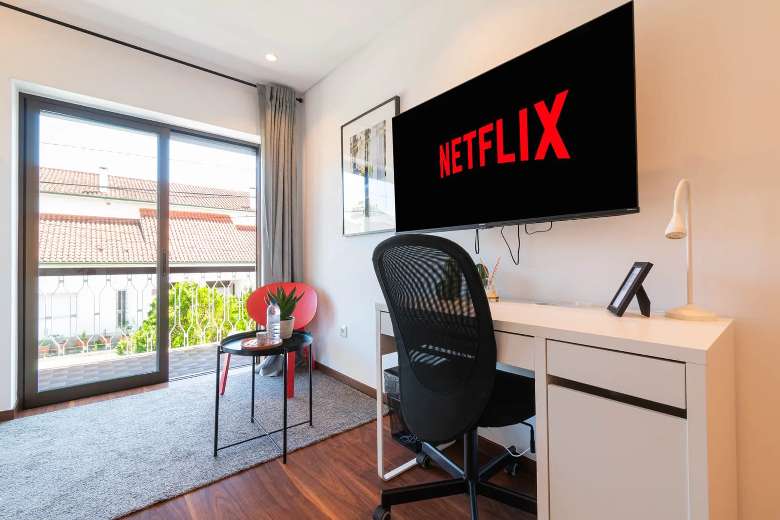 Compact desk corner with TV and balcony glimpse to neighborhood