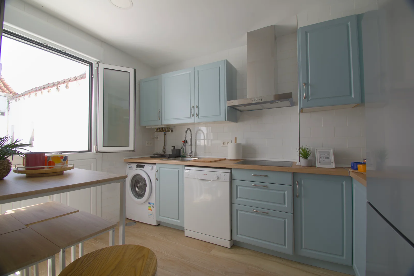 Daylit kitchen window framing pale-blue cabinets and breakfast bar