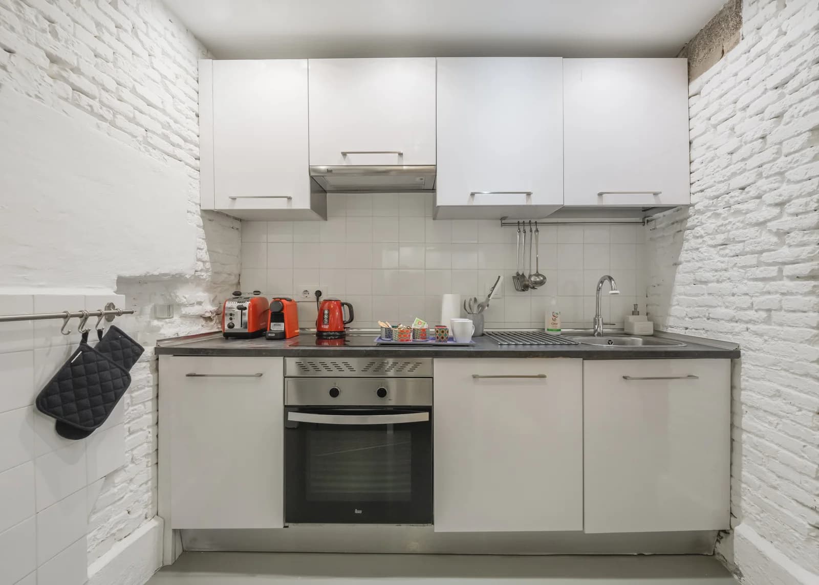 Compact white kitchen with whitewashed brick walls and pop-orange appliances