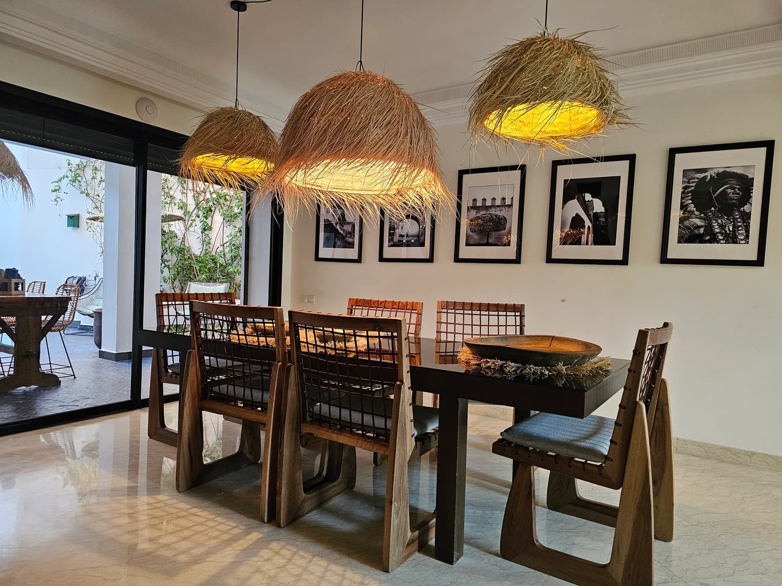 Dining table under rattan pendants beside black-and-white photography wall